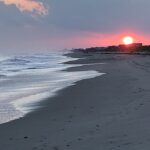 Ocean shoreline at sunset with waves and glowing horizon – seascape photography by Layne Morgan