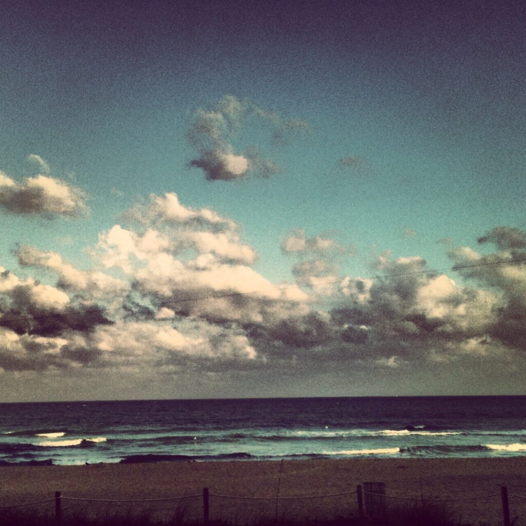 Clouds above calm ocean horizon with birds – fine art sky photography by Layne Morgan