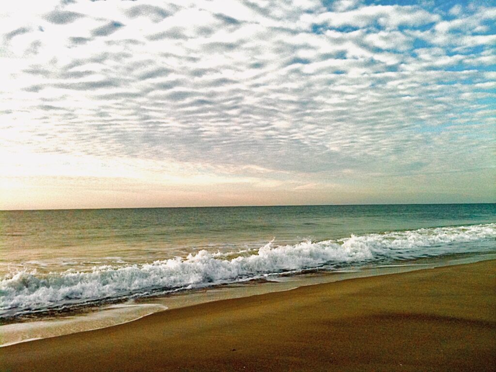 Ocean waves rolling onto a sandy beach beneath a textured cloud-filled coastal sky