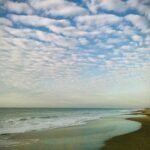 Ocean waves along a sandy shoreline beneath a dramatic cloud-filled coastal sky