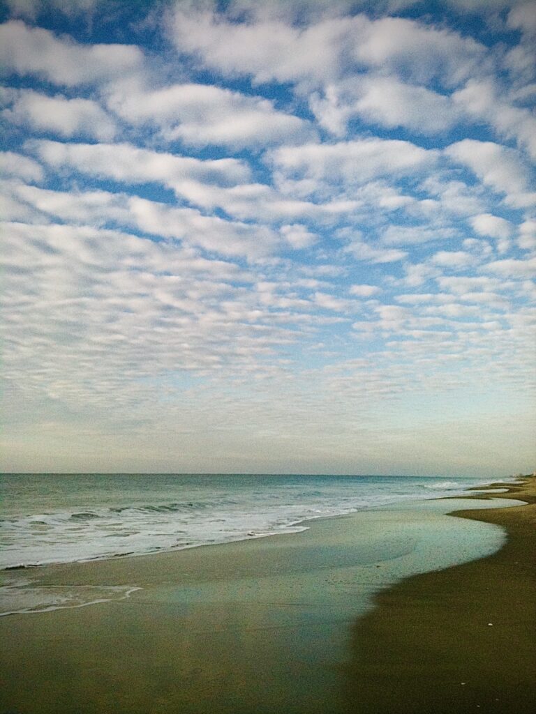 Ocean waves along a sandy shoreline beneath a dramatic cloud-filled coastal sky