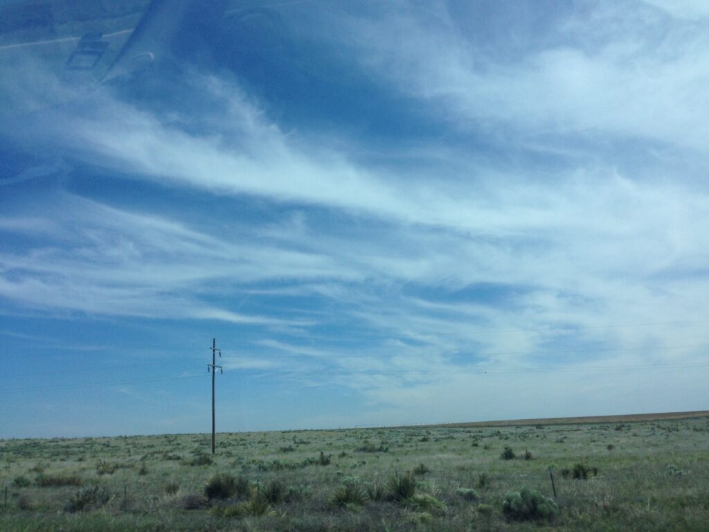 Wispy clouds across blue sky above open landscape – fine art cloudscape photography by Layne Morgan