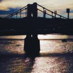 Suspension bridge silhouette over water at sunset fine art architectural photography by Layne Morgan
