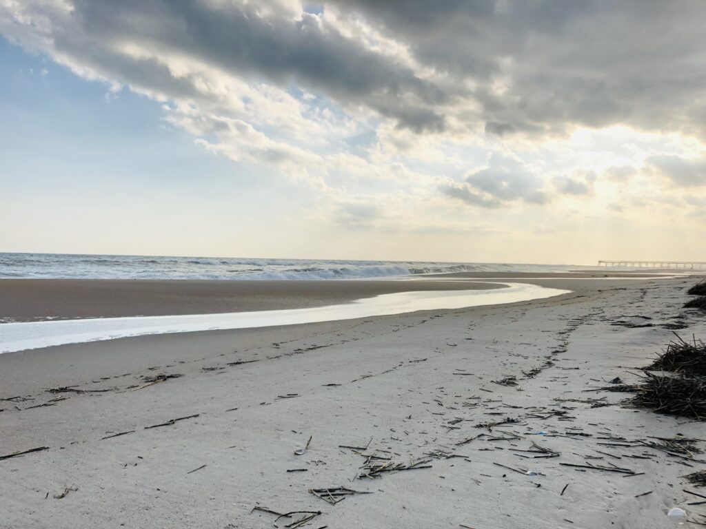 Sunlight breaking through clouds above a quiet coastal shoreline and ocean waves