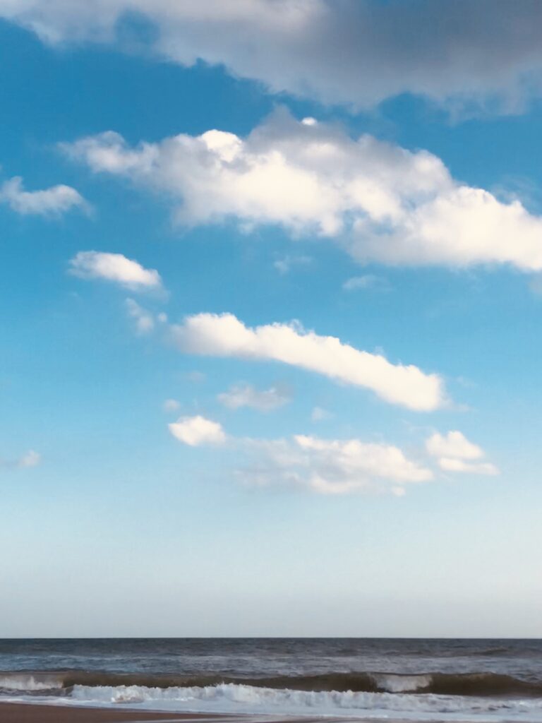 Bright blue sky with white clouds above a calm coastal ocean horizon