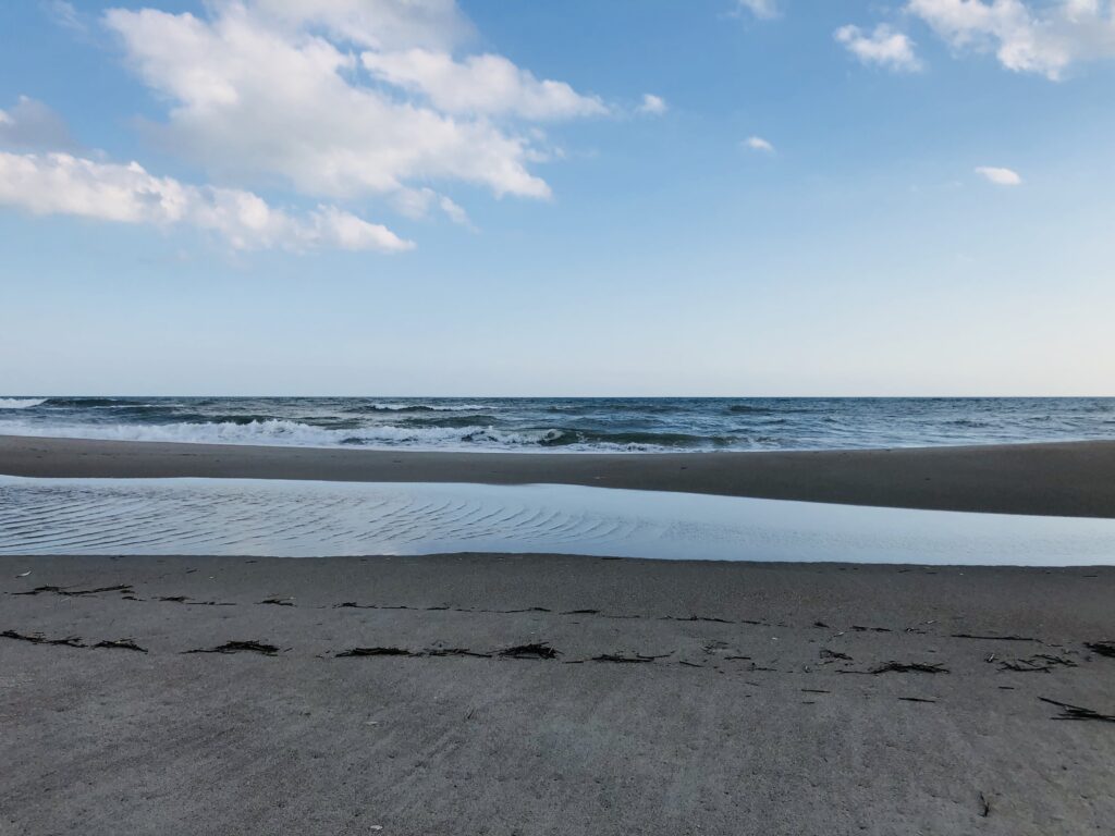 Wide sandy beach shoreline with blue sky and calm ocean horizon