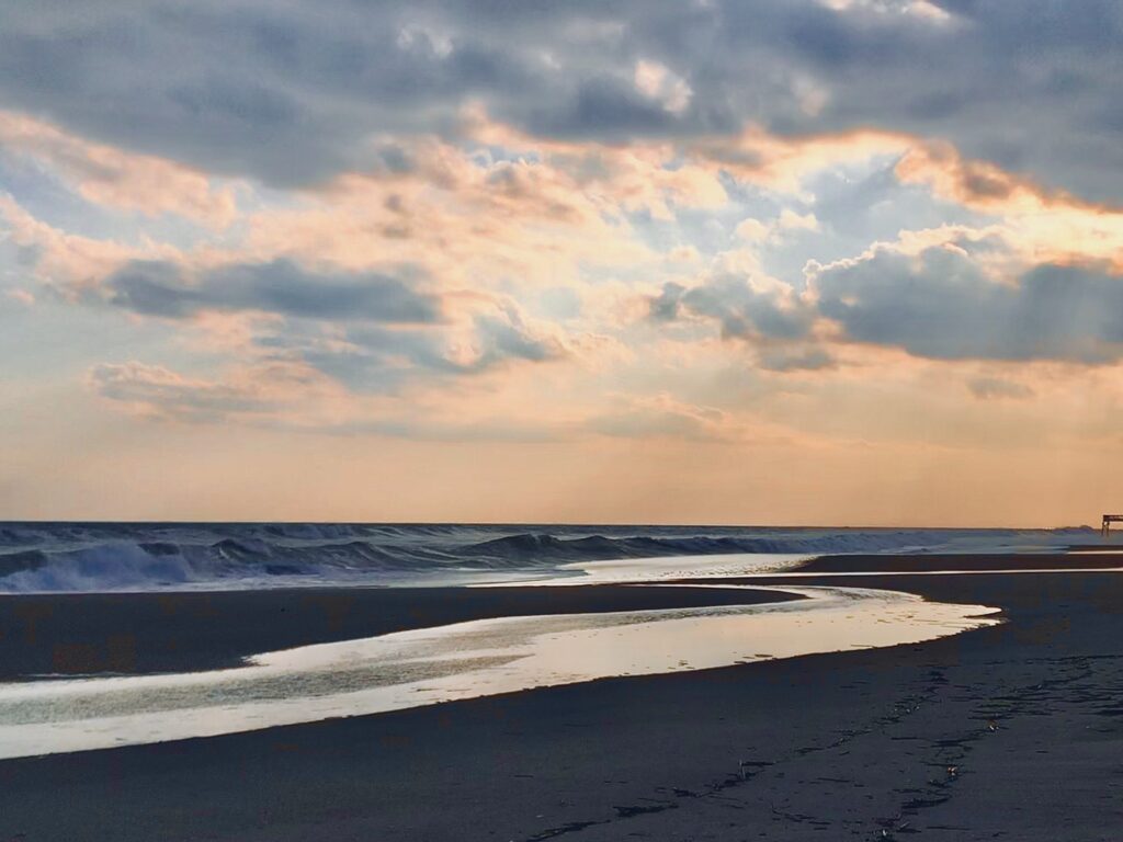 Sunset clouds glowing above a quiet beach shoreline and ocean horizon