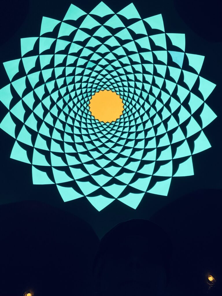 Symmetrical geometric mandala pattern with teal shapes and a glowing yellow center on dark background